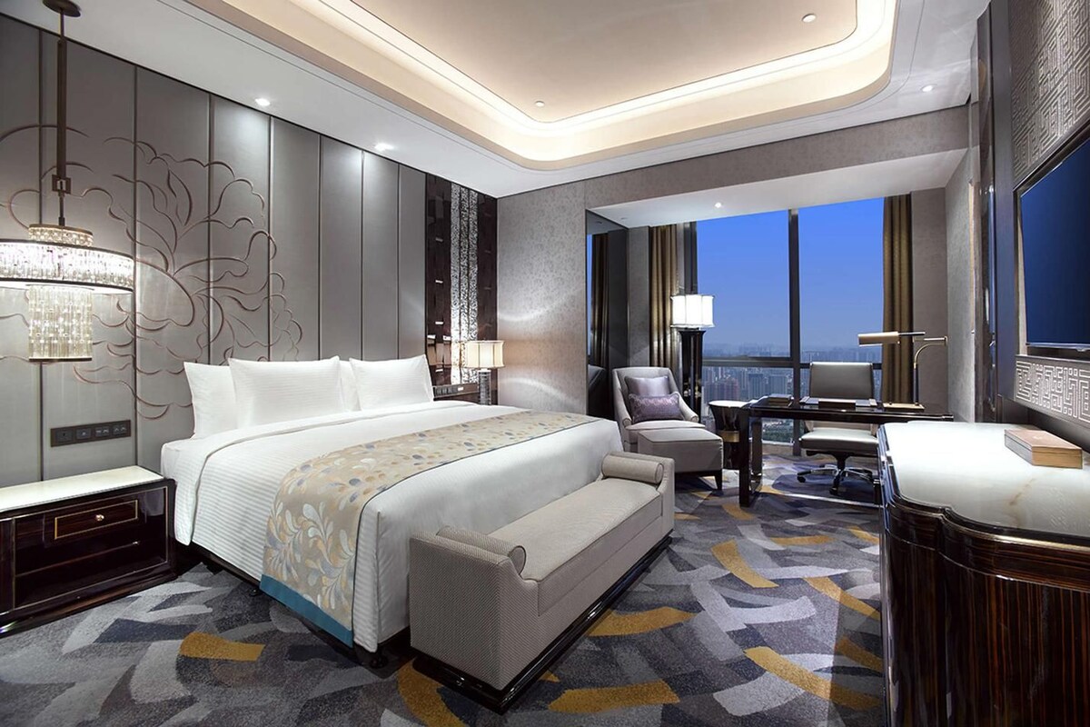 Une chambre d’hôtel moderne avec un grand lit, un bureau, une chaise et une vue sur le paysage urbain.
