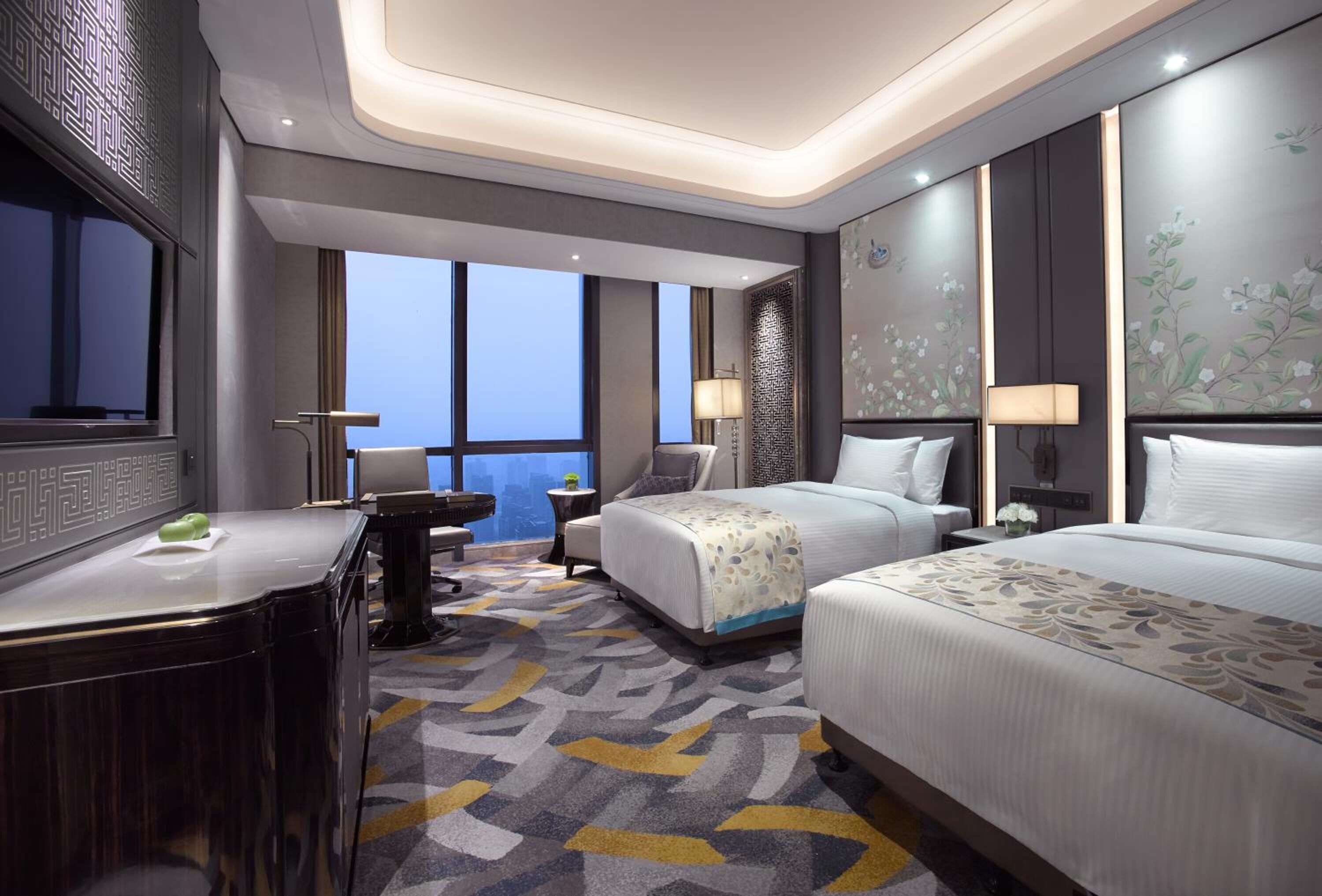 Ein modernes Hotelzimmer mit zwei Betten, einem Schreibtisch und Blick auf die Stadt.