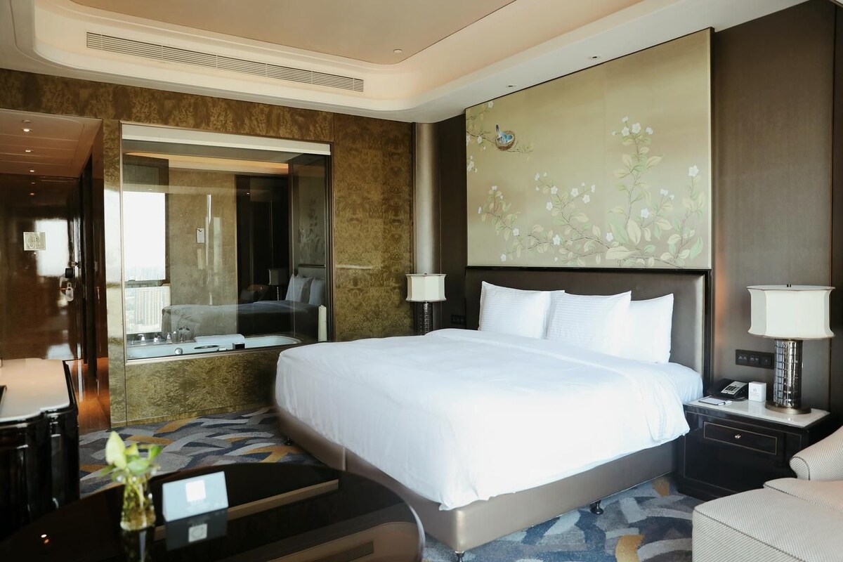 Une chambre d’hôtel avec un grand lit, un miroir, une table de chevet avec une lampe et un mur décoré d’œuvres d’art florales.