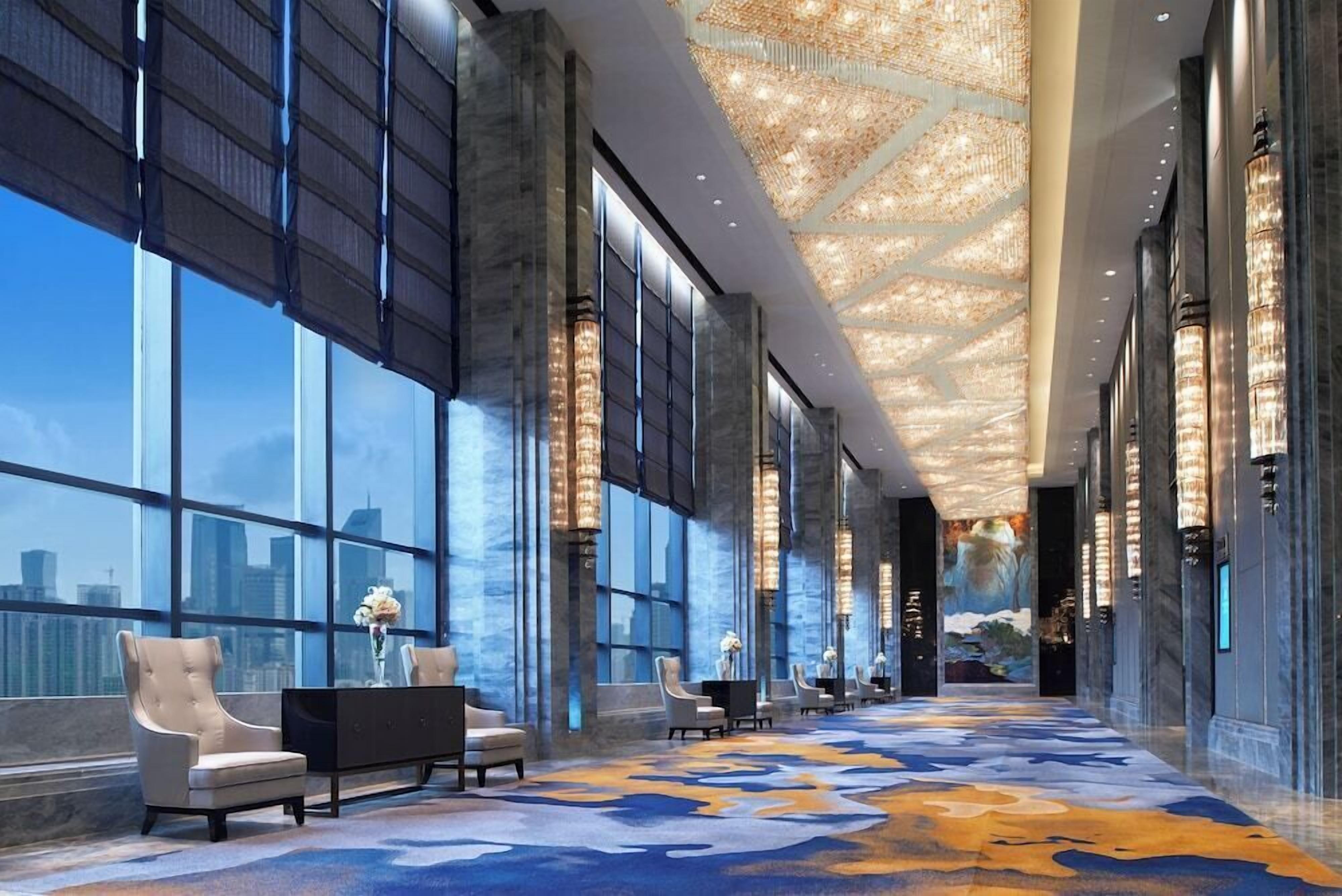 A spacious lobby with large windows, a patterned carpet, and a chandelier.