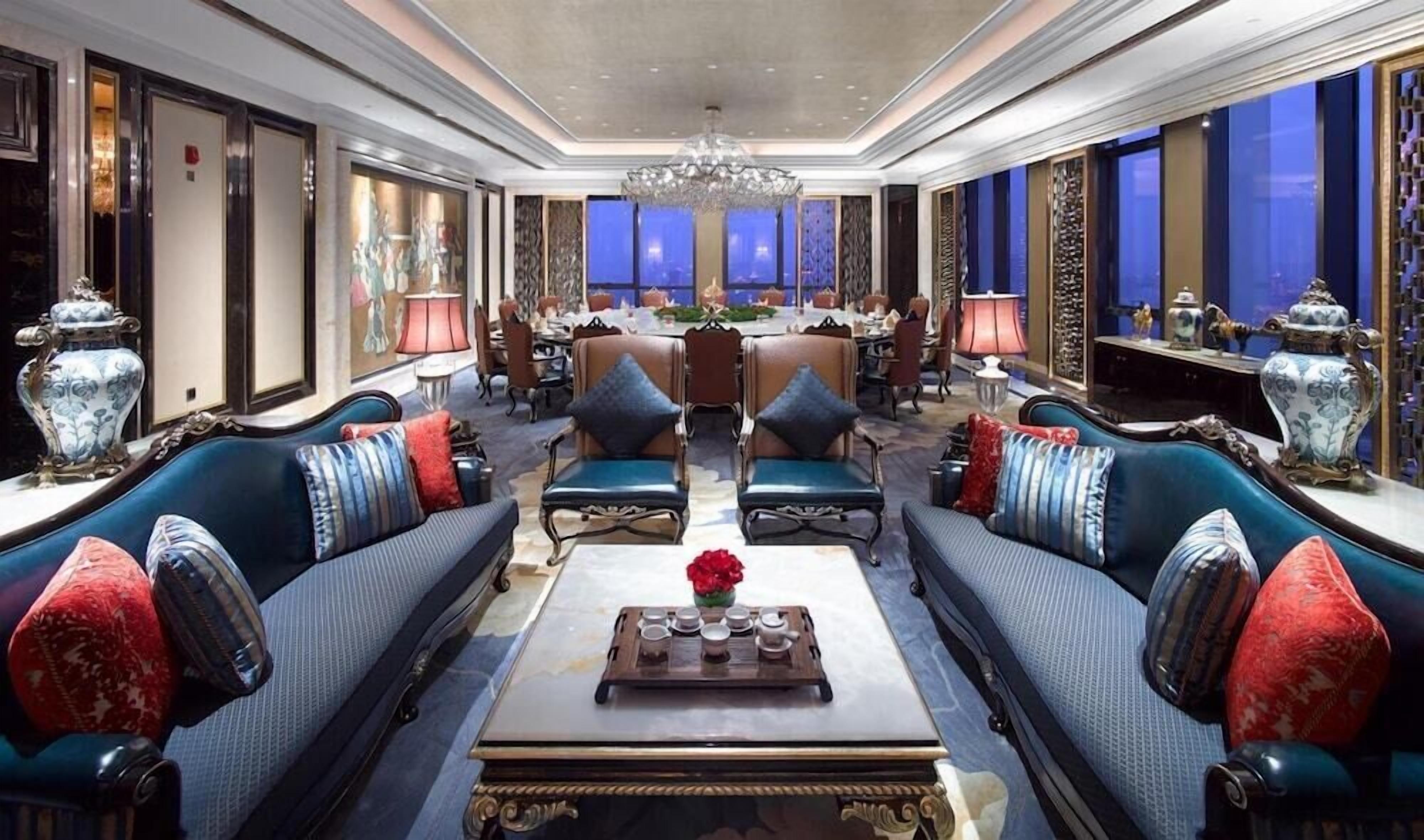 Un hall d’hôtel luxueux, doté d’un espace salon central, d’une décoration raffinée et de grandes fenêtres.