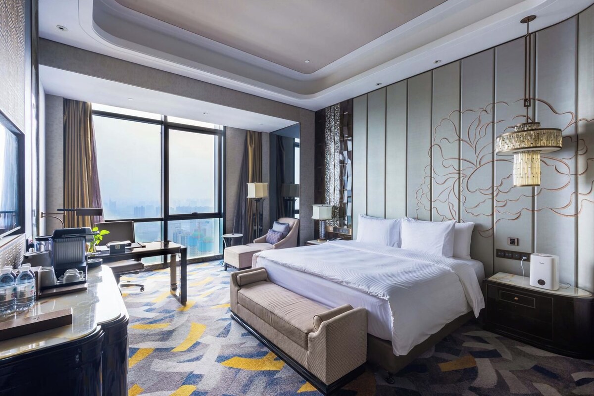 Une chambre d’hôtel avec un grand lit, un bureau avec une chaise, un canapé, une table de chevet et une lampe.