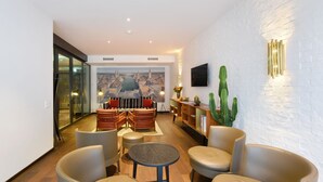 Una sala moderna con un mural de paisaje urbano, sofás de cuero, una mesita redonda y una planta de cactus.