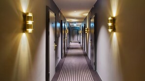 Un pasillo de hotel con alfombra a rayas, puertas e iluminación empotrada en la pared.