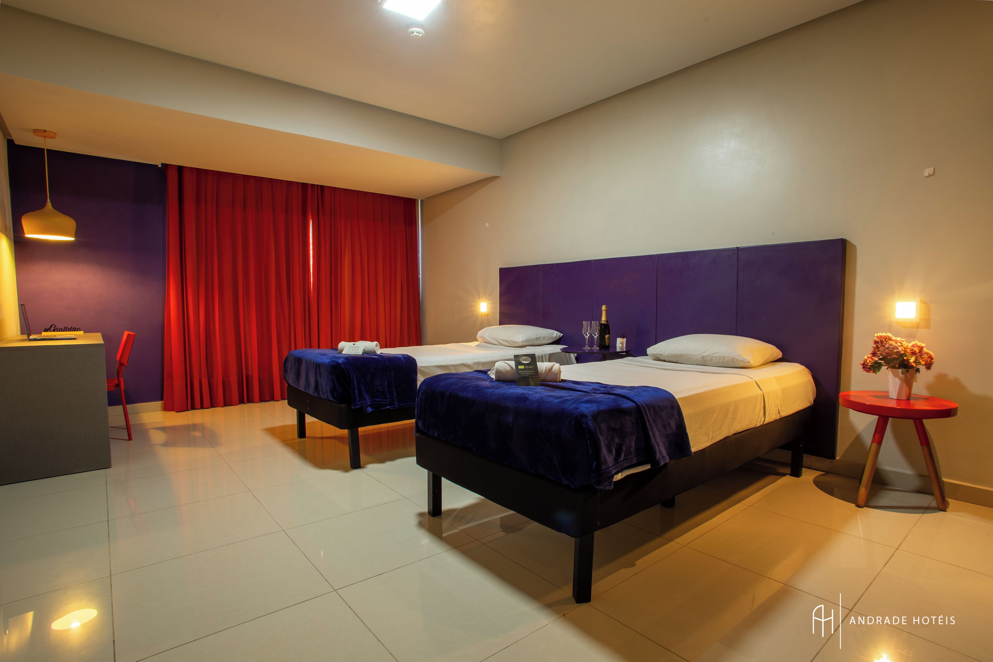 Habitación de hotel con dos camas, un escritorio y una cortina roja.