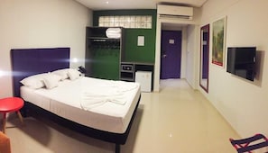 Une chambre d’hôtel avec un lit, une chaise rouge, un bureau avec un ordinateur, une armoire et un téléviseur.