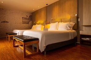 A modern hotel room with a large bed, a wooden bench, and a textured wall with a sign. - QUO Quality Hotel (MANIZALES)