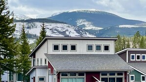 A two-story house with a garage, a covered porch, and a mountain backdrop.