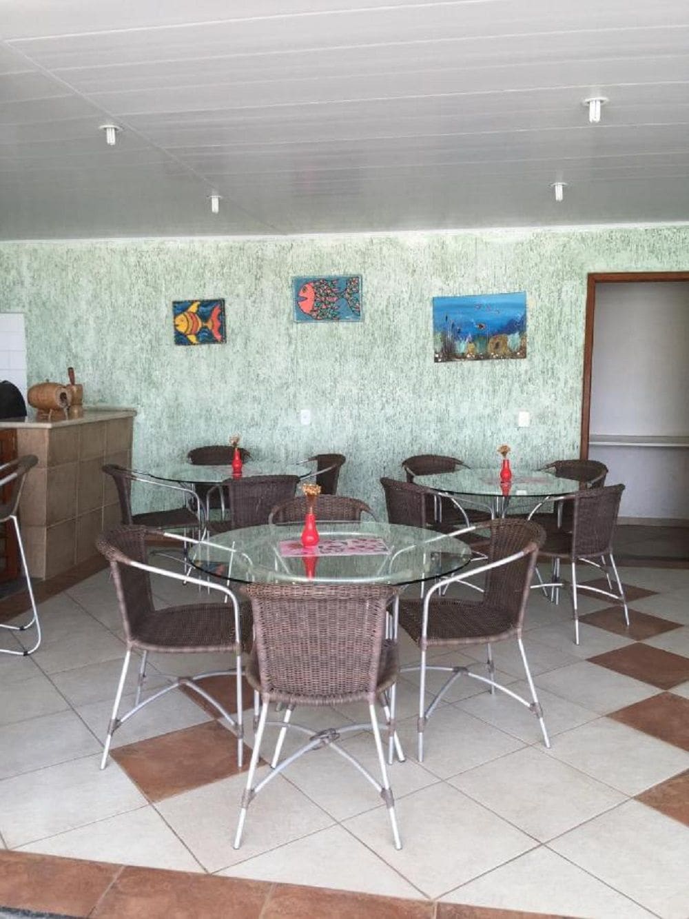 A dining area with round glass tables and wicker chairs, a tiled floor, and artwork on the walls.
