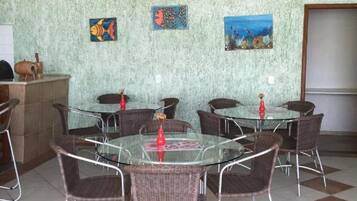 A dining area with round glass tables and wicker chairs, a tiled floor, and artwork on the walls.