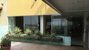 Entrada de un edificio con un patio adoquinado, plantas en macetas y una puerta de vidrio.