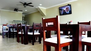 Un comedor con mesas y sillas de madera, un televisor montado en la pared y ventiladores de techo.