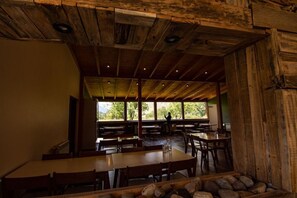 A rustic dining area with wooden tables and benches, large windows offering a view of greenery outside. - Fitz Roy Inn (El Chalten)