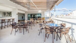 A rooftop bar with wicker furniture, a glass table, and a view of the city skyline. - Victory Suites (Juiz de Fora)