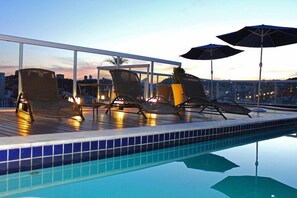 A rooftop pool area with lounge chairs and umbrellas, overlooking a cityscape at dusk. - Victory Suites (Juiz de Fora)