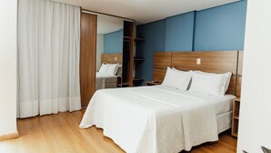 A modern hotel room with a large bed, wooden headboard, and a wardrobe with a mirror. - Victory Suites (Juiz de Fora)