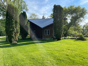 A wooden cabin with a metal roof, surrounded by lush green grass and trees.