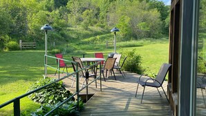 A wooden deck with outdoor furniture, a glass door, and a view of a green landscape. - Upper Place Vacation Cottage (Gays Mills)