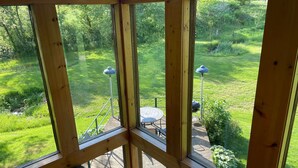 A wooden deck with a table and chairs, surrounded by a lush green garden. - Upper Place Vacation Cottage (Gays Mills)