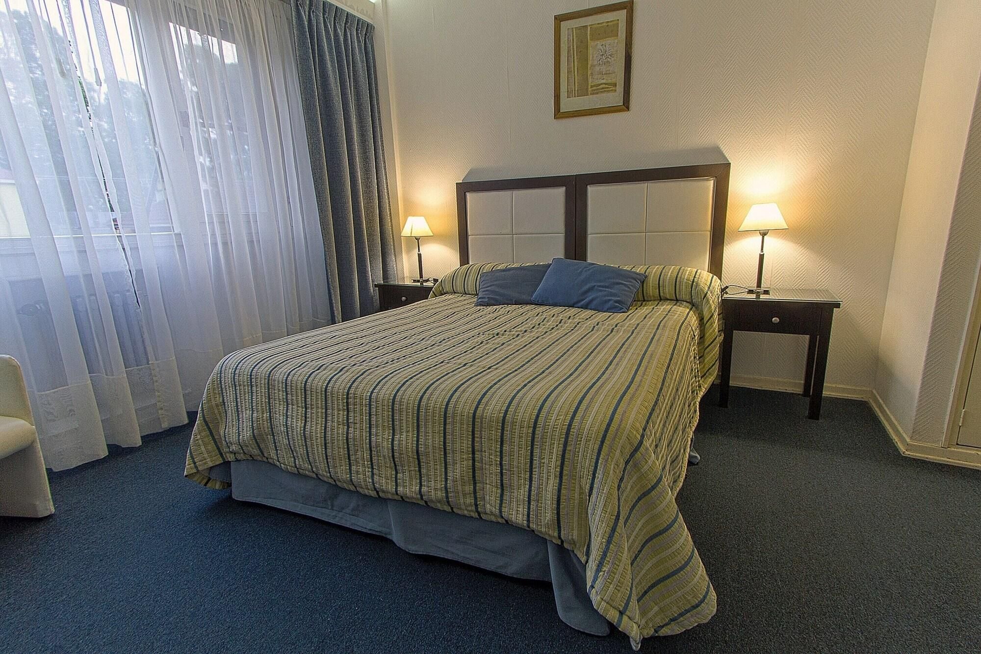 A hotel room with a large bed, two bedside tables with lamps, a chair, and a window with curtains.