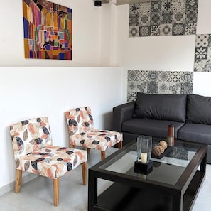 A modern living room with a black sofa, two patterned armchairs, a glass coffee table, and a decorative wall with tile patterns. - Hotel Libertador Pinamar (Pinamar)
