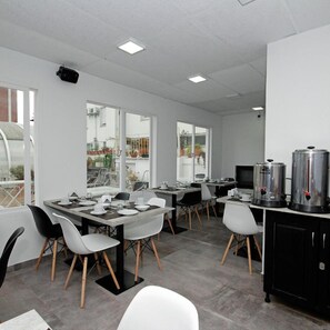 A modern dining area with tables and chairs, large windows, and a kitchen area with appliances. - Hotel Libertador Pinamar (Pinamar)