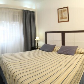 A hotel room with a bed, curtains, a lamp, and a framed picture on the wall. - Hotel Libertador Pinamar (Pinamar)