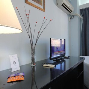 A hotel room with a flat-screen TV, a vase with branches, a remote control, and a lamp on a table. - Hotel Libertador Pinamar (Pinamar)
