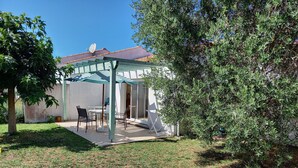 Un patio couvert avec une table et des chaises, une pergola et une vue sur un bâtiment équipé d’une antenne parabolique.