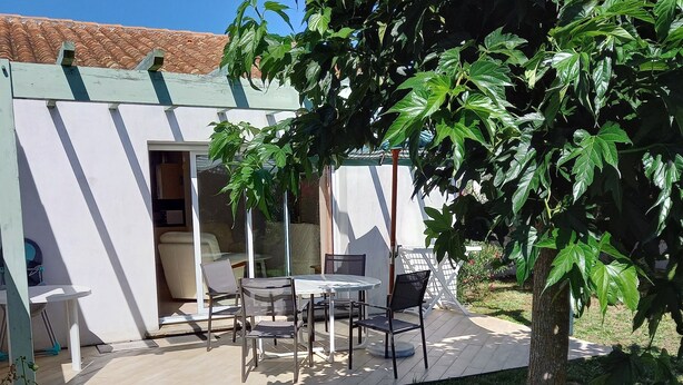 Un espace extérieur aménagé avec une table et des chaises, un coin salon abrité et un bâtiment doté d’une porte et de fenêtres.