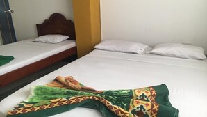 Una habitación con dos camas individuales, cada una con ropa de cama y almohadas blancas. Se observa un cabecero de madera en la cama de la izquierda y una pared amarilla a la derecha.