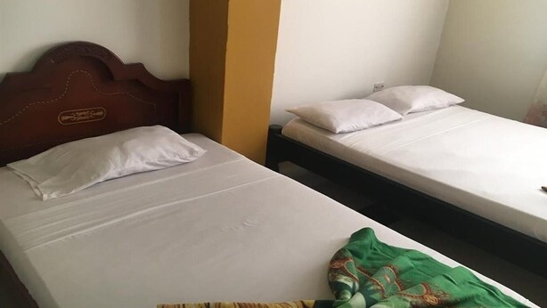 Dos camas individuales con sábanas blancas, un cabecero de madera y una manta verde en el suelo.