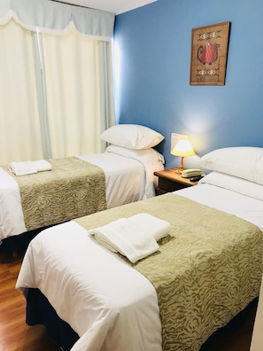 Habitación de hotel con dos camas, una mesita de noche con lámpara y un cartel en la pared.