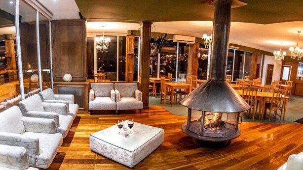 Una sala de estar acogedora con chimenea en el centro, asientos mullidos y una zona de comedor con muebles de madera.