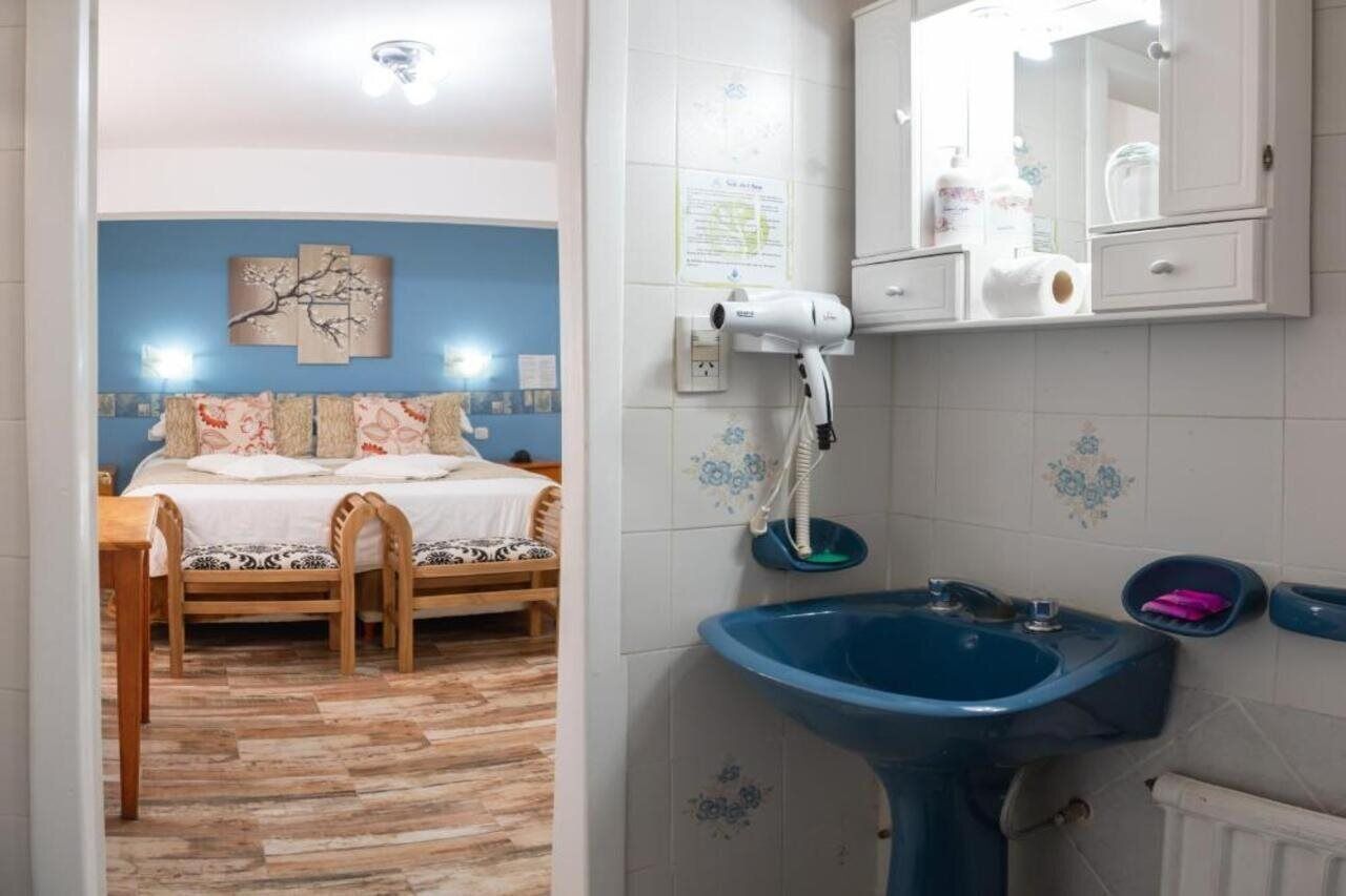 A bedroom with a bed, a wooden chair, a blue sink, and a mirror above the sink.