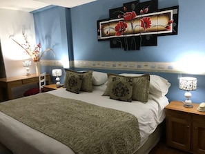 Un dormitorio con cama, mesitas de noche, lámparas y una obra de arte en la pared.