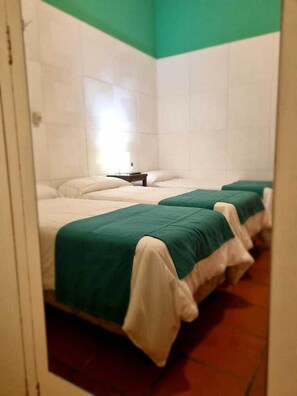 Une chambre avec trois lits, chacun recouvert d’une couverture verte et blanche, et une petite table placée entre les lits.