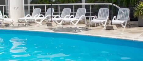 A swimming pool with white lounge chairs and umbrellas.