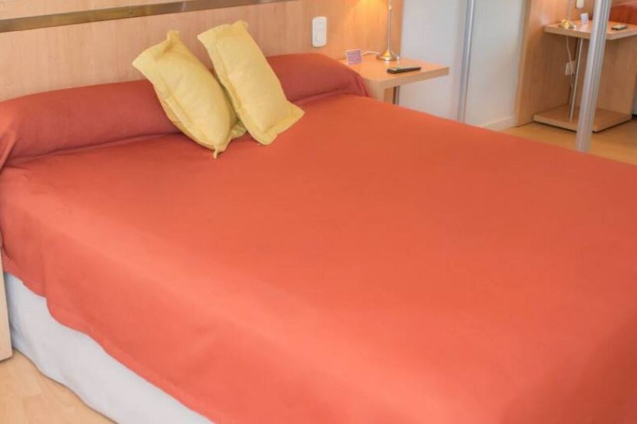 A hotel room with a bed, a nightstand, a lamp, and a small table.