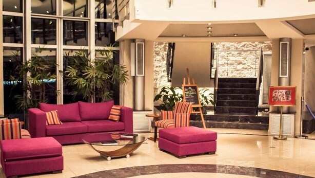 A lobby with a purple sofa set, a coffee table, and striped chairs. There are potted plants and a staircase in the background. - Maran Suites And Towers (Parana)
