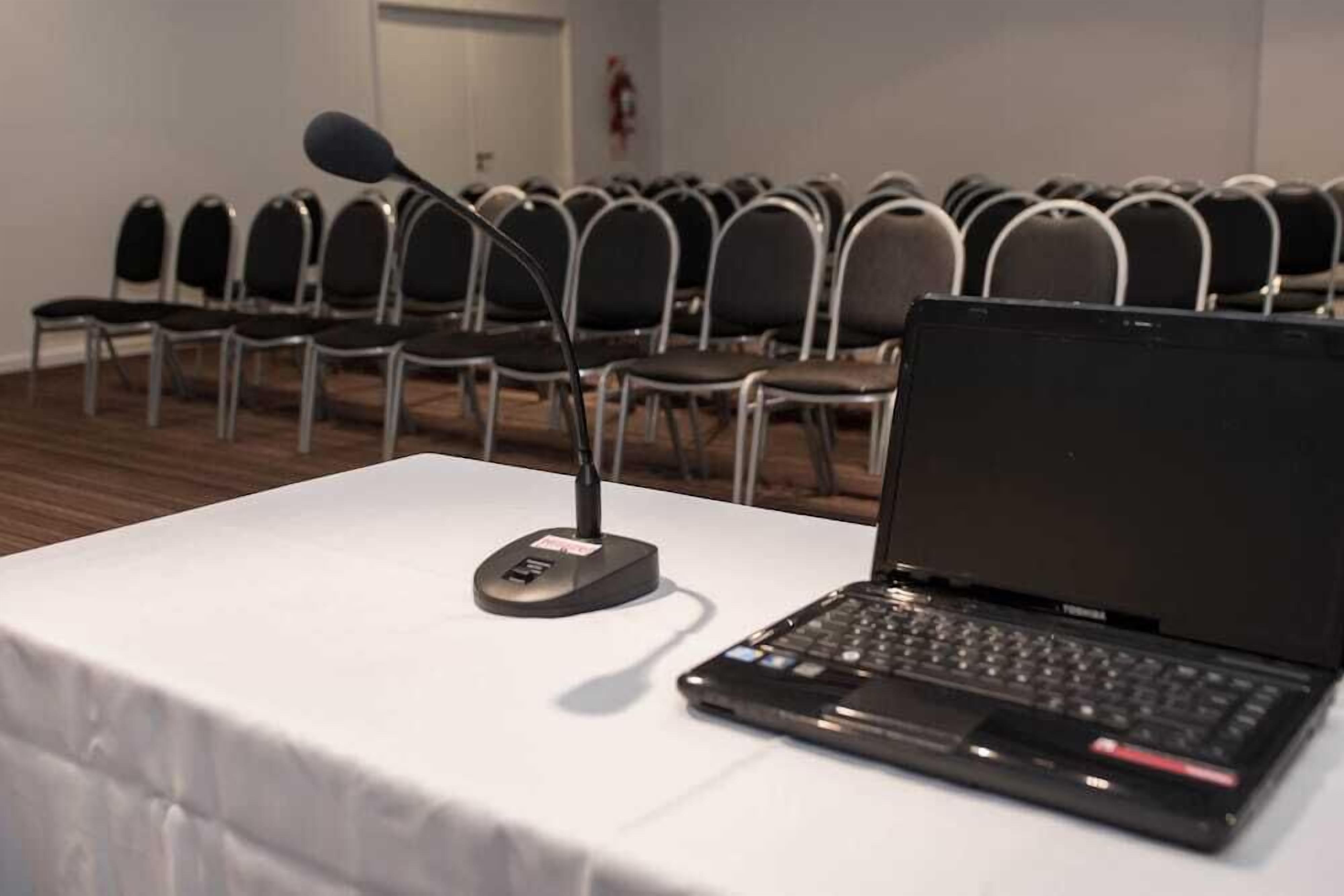 Un salón de conferencias con filas de sillas, una computadora portátil y un micrófono sobre una mesa.