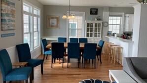 Ein Essbereich mit Holztisch und blauen Stühlen, eine Küche mit weißen Schränken sowie ein Wohnbereich mit einer Couch und einem gemusterten Teppich.