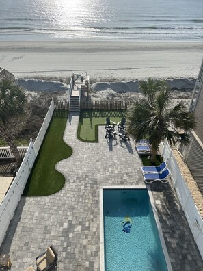 Zona de piscina con vista a la playa, una pequeña terraza y sillas de descanso.