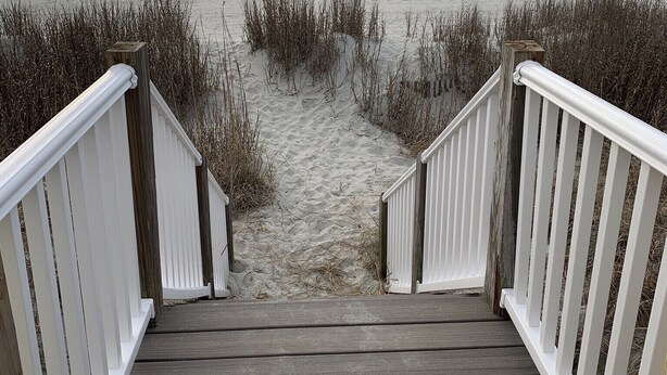 Eine Holztreppe führt zu einem Strand mit Blick auf das Meer.
