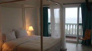 A four-poster bed with white linens, a bedside lamp, and a view of the sea through a balcony with blue curtains. - Aria Hotel Spa (Cartagena)