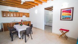 A dining area with a table and chairs, a kitchen with wooden cabinets, and a painting on the wall. - Aria Hotel Spa (Cartagena)