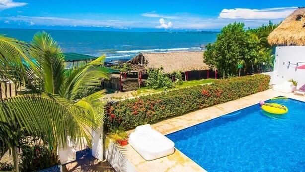 A pool area with a view of the ocean, a thatched-roof structure, and a white building with a balcony. - Aria Hotel Spa (Cartagena)
