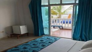 A hotel room with a bed, a small table, a chair, and a view of the beach through a glass door. - Aria Hotel Spa (Cartagena)