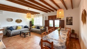 A spacious living room with a large dining table, two sofas, wooden beams on the ceiling, and a hanging plant. - Villa Hugo Cómpeta by Ruralidays (Málaga)