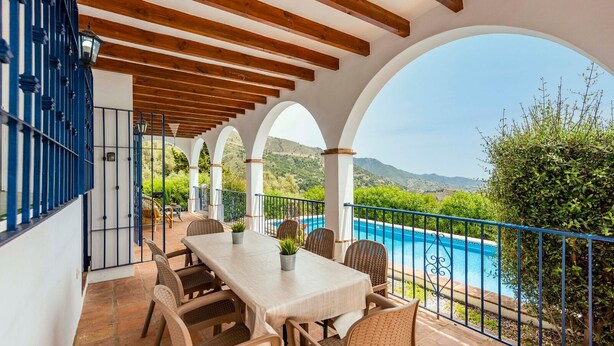 A covered outdoor dining area with a pool view, featuring a table and chairs, and a railing overlooking a pool. - Villa Hugo Cómpeta by Ruralidays (Málaga)